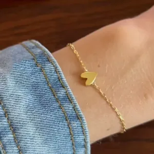 Detailed close-up of a delicate gold heart pendant bracelet worn on a female wrist