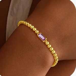Gros plan d'un bracelet en perles dorées avec une pierre rectangulaire violette au poignet