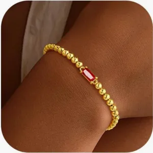 Détail d'un bracelet en perles dorées avec zircon rouge rectangulaire sur poignet de femme