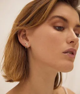 Détail de boucles d'oreilles croisées dorées minimalistes serties de zircons brillants