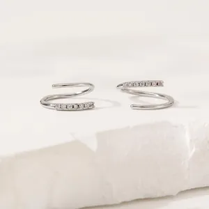 Elegant silver spiral hoop earrings with pavé white zircon stones on stone background
