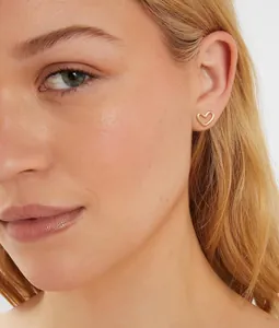 Gros plan d'un modèle portant une boucle d'oreille cœur dorée avec une finition polie
