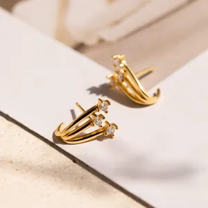 Detalle macro de pendientes dorados de tres filas con cristales cuadrados