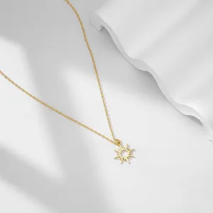 Dettaglio di un ciondolo a forma di sole dorato su una catena sottile su sfondo bianco