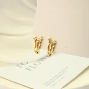 Vista macro de pendientes de lazo dorado con circonitas cuadradas en tarjeta expositora