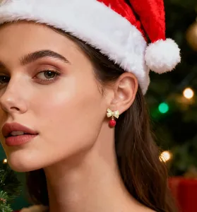 Primer plano de pendientes de lazo navideño con perla roja en modelo con decorado festivo