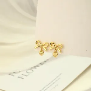 Primer plano de pendientes de lazo dorado con colgante de corazón en tarjeta