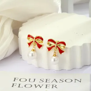 Detalle de pendientes de lazo de esmalte rojo con perlas blancas en un soporte blanco