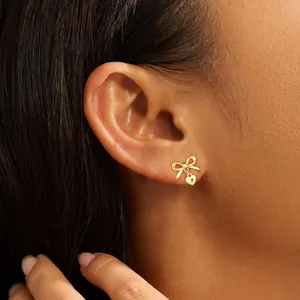 Detalle de pendientes de lazo con colgantes de corazón en acabado dorado pulido en la oreja