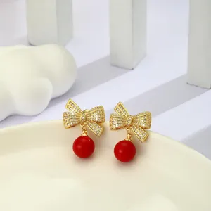 Detalle de pendientes de lazo dorado con cristales y cuentas rojas en soporte blanco