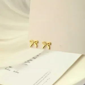 Vista macro de pendientes de lazo dorado en tarjeta beige y bandeja de cerámica