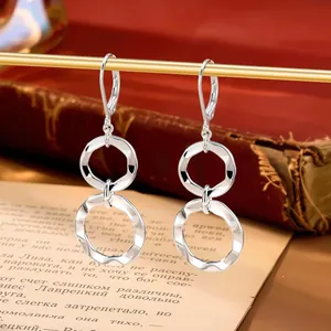Gros plan de boucles d'oreilles argentées à double anneau ondulé sur fond vintage