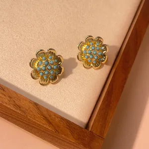 Detailed macro view of gold-plated flower stud earrings with turquoise beaded center