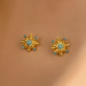 Detail of gold-plated sunburst stud earrings with turquoise stones on orange background