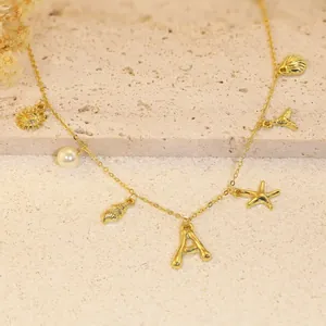 Detail of gold-plated bamboo necklace with shell, pearl, and letter A charms on sand