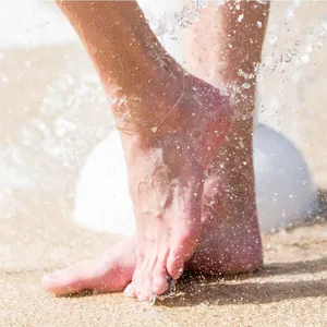 Cavigliera doppia in oro con ciondolo a cuore sulla spiaggia con spruzzi d'acqua