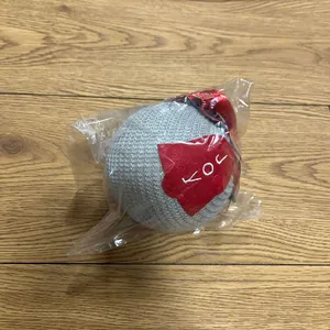 Detail of grey knitted Christmas ornament ball with red tree tag and hanging rope in package