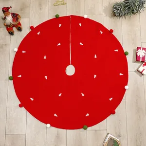 Red Christmas tree skirt with white embroidery and colorful pom-poms on wooden floor