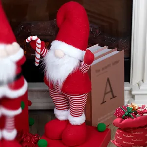 Standing Christmas gnome with red hat, white beard and candy cane by a fireplace
