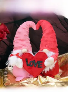 Detail of plush Valentine gnomes holding a red LOVE heart against a rose background