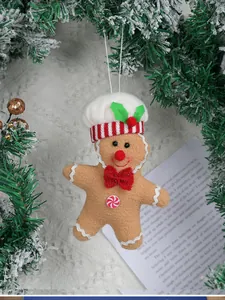 Detail of plush gingerbread man ornament with chef hat hanging on snowy Christmas tree