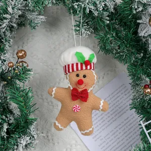 Gingerbread man plush ornament with chef hat hanging on snow-covered pine branch