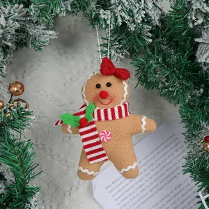 Gingerbread man plush ornament with red bow on snowy Christmas tree branch