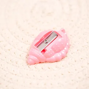 Pink shell-shaped manual pencil sharpener made of plastic on a beige woven surface
