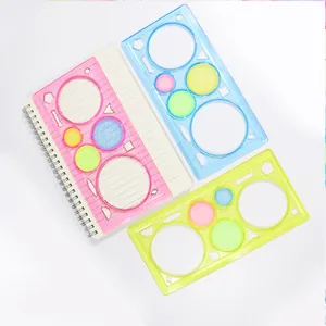 Trois règles spirographe colorées en plastique posées sur un carnet blanc à spirales