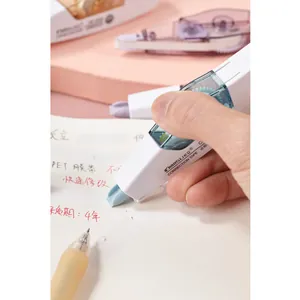 Gros plan d'un ruban correcteur blanc tenu à la main sur du papier avec texte manuscrit