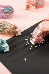 Hand mit rosa Kleberoller erzeugt glatte gepunktete Klebelinien auf schwarzem Papier