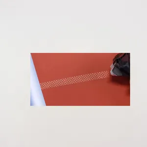 Détail du ruban adhésif doré à motifs dentelle sur papier rouge avec dévidoir noir