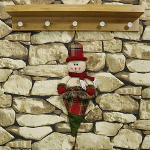 Christmas snowman plush hanging decoration with red scarf and checkered hat on stone wall