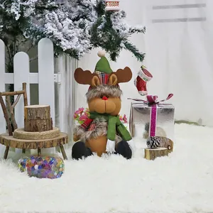 Cute Christmas reindeer plush doll with green knit hat and scarf on a snowy white rug
