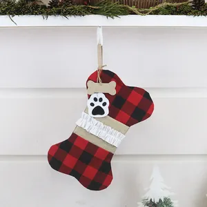 Hundeknochen-Weihnachtssocke mit Karomuster und Pfotenabdruck vor weißem Kamin