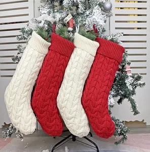 Close-up of red and beige cable knit Christmas stockings hanging on a snow-covered tree
