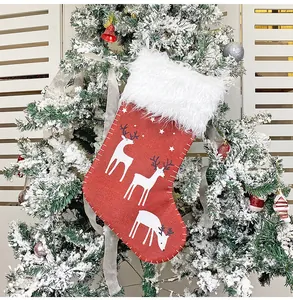 Detail eines roten Weihnachtsstrumpfs mit Rentierdruck und weißem Plüschrand am Baum