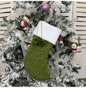 Detail of green knitted Christmas stocking with white faux fur cuff and plush pom poms