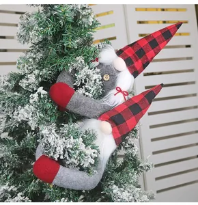 Close-up of plush Christmas gnome ornaments with red plaid hats hanging on a snowy tree