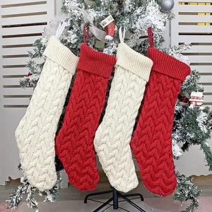 Set of four knitted Christmas stockings with cable patterns hanging on a snowy festive tree