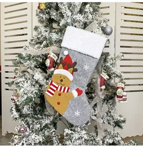 Detailed view of grey felt Christmas stocking with reindeer doll hanging on snowy tree