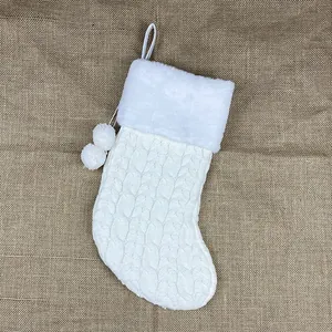 White cable knit Christmas stocking with faux fur trim and pom-poms on burlap background