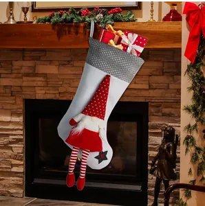 Detail van een witte kerstsok met een 3D-kabouterpop en geschenkdozen bij een open haard