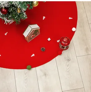 Close-up of red Christmas tree skirt with colorful pom-poms and white tree patterns
