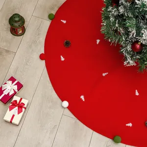 Red Christmas tree skirt with festive pom-poms and white tree patterns on wood floor