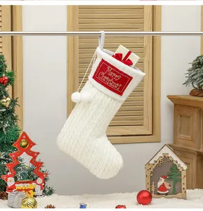 Detail van gebreide witte kerstsok met rode Merry Christmas borduring en pompons