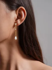 Primer plano de pendientes dorados con borlas y perlas de gota en una modelo mujer