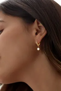 Primer plano de pendientes de aro en latón dorado con cristales pavé y una pequeña perla blanca