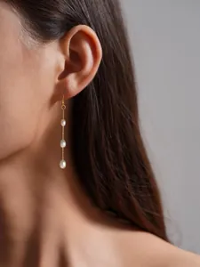 Detalle de pendientes de perlas con cadena dorada lucidos por una modelo