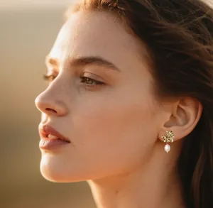 Primer plano de pendientes de flores doradas con perlas blancas en una modelo